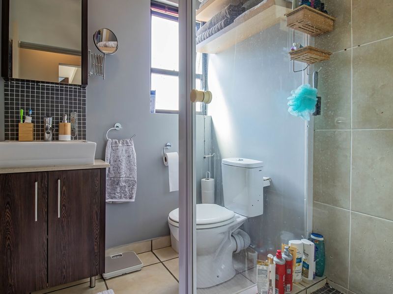 A functional bathroom featuring a dark wood vanity with a vessel sink, mosaic backsplash, toilet, and a glass-enclosed shower with built-in shelving.