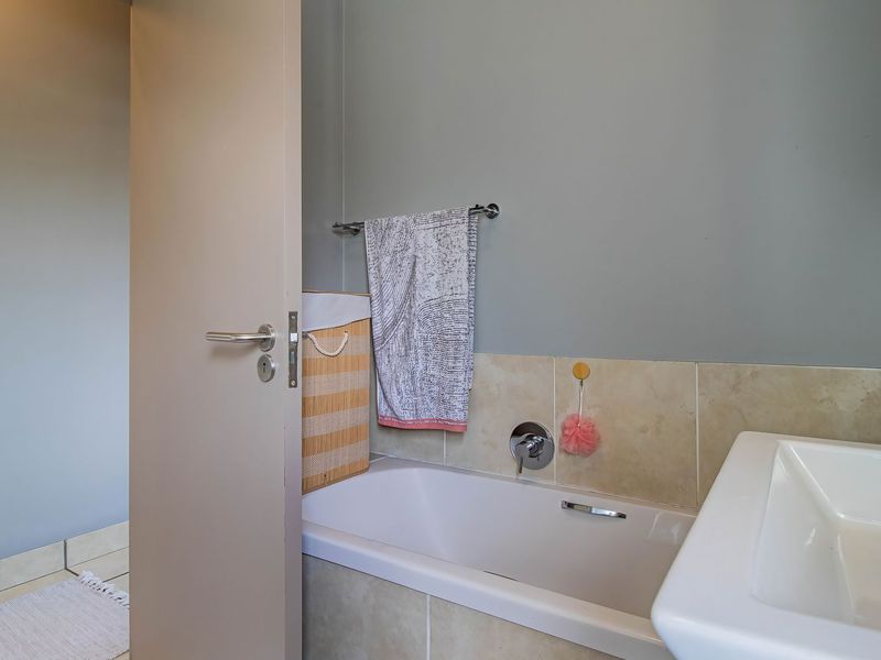 A functional bathroom featuring a bathtub with a shower mixer, tiled splashback, and a wall-mounted washbasin.