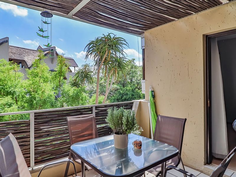 A covered balcony featuring a bamboo privacy screen, textured walls, and tiled flooring, offering a pleasant outdoor space with views of the surrounding greenery.