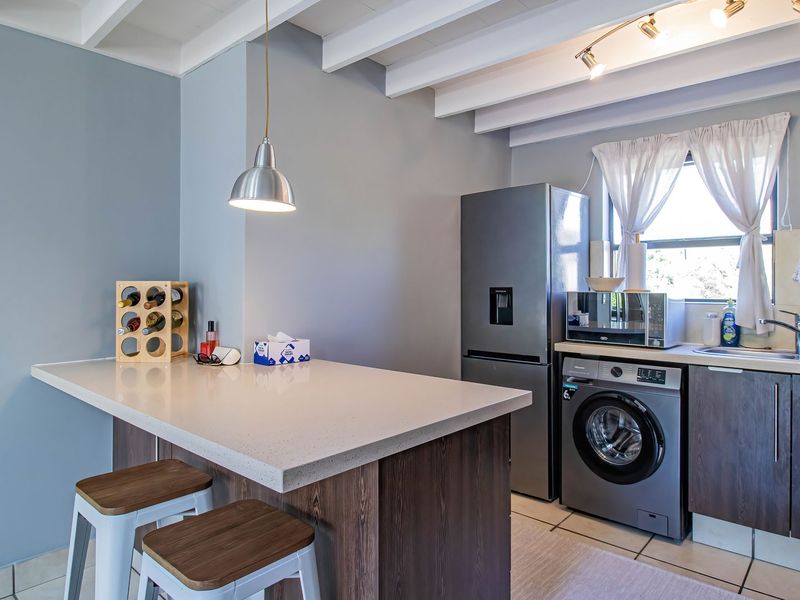 Modern kitchen featuring stone countertops, dark wood cabinetry, exposed white ceiling beams, and integrated laundry and kitchen appliances.