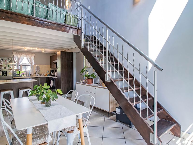 Open-plan living and dining area featuring a mezzanine level, modern staircase with metal balustrade, tiled flooring, and a functional kitchen with built-in cabinetry.