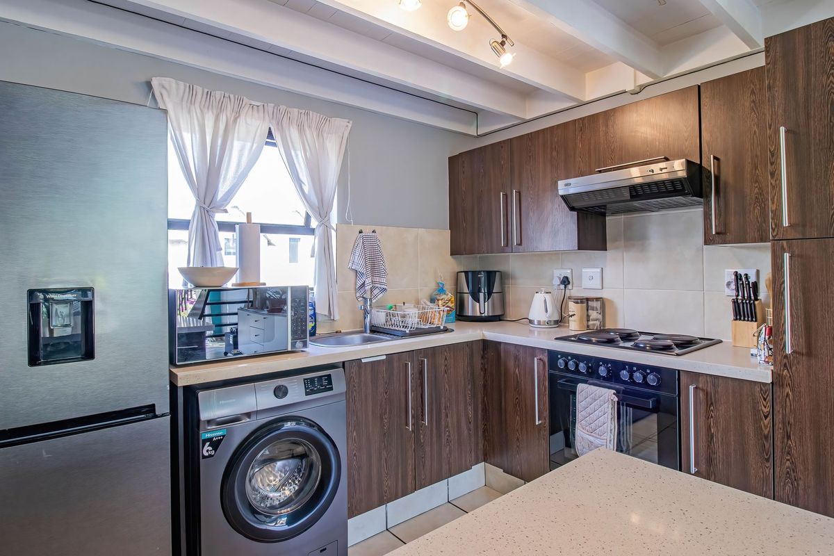 A functional kitchen featuring dark wood-grain cabinetry, stone-look countertops, built-in oven with hob, and exposed ceiling beams for a modern aesthetic.