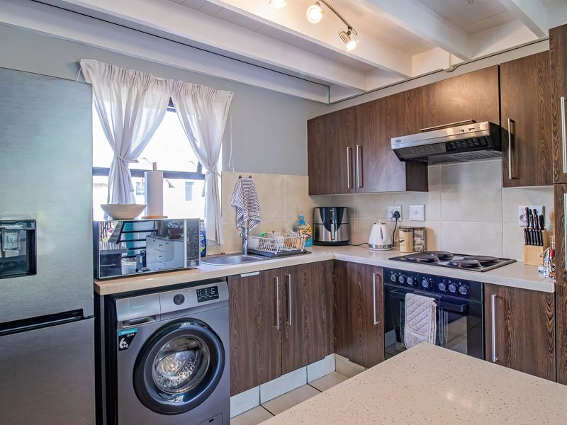A functional kitchen featuring dark wood-grain cabinetry, stone-look countertops, built-in oven with hob, and exposed ceiling beams for a modern aesthetic.