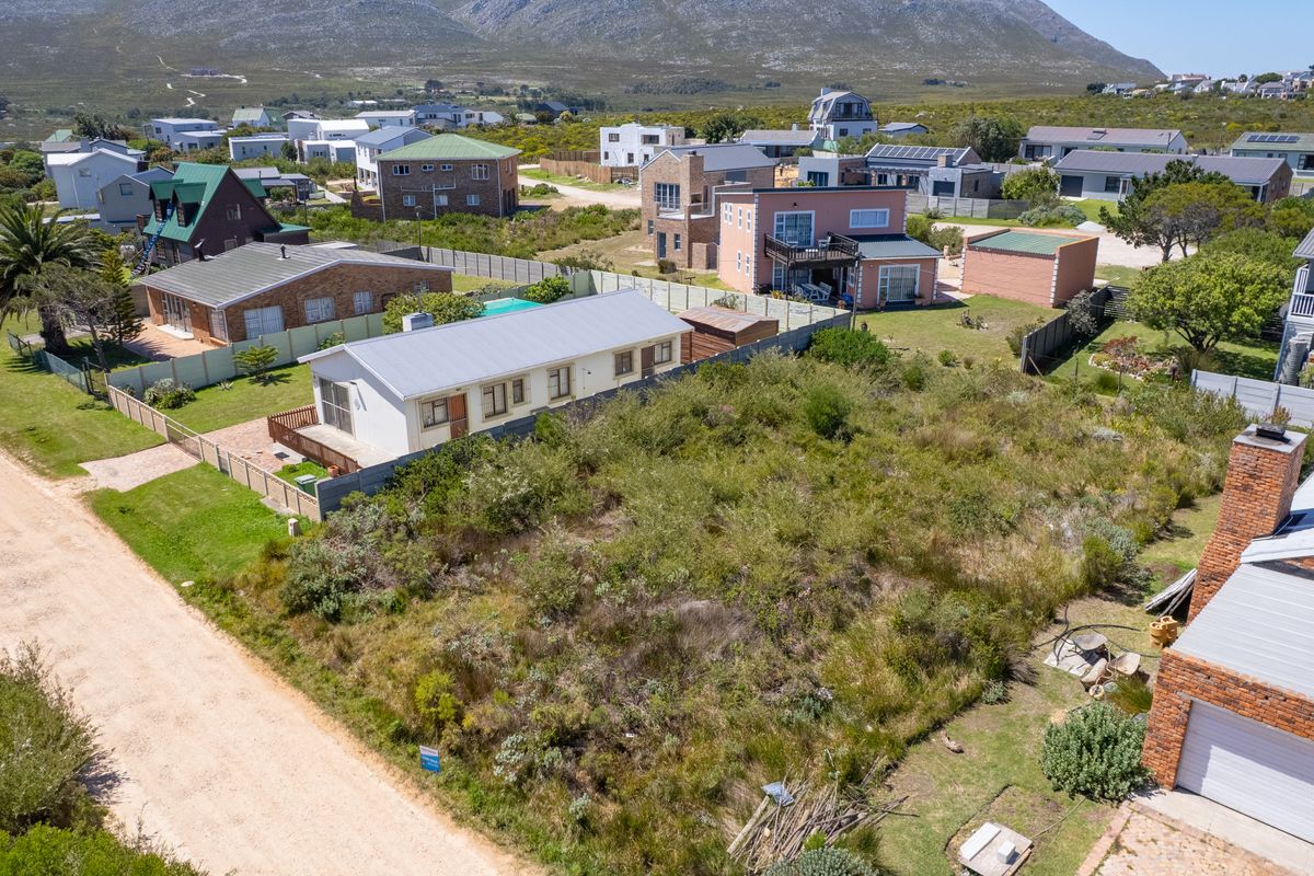 Aerial view of a vacant residential plot situated in a developed coastal neighborhood with mountain views and unpaved road access.