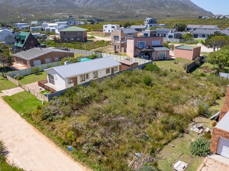 Aerial view of a vacant residential plot situated in a developed coastal neighborhood with mountain views and unpaved road access.