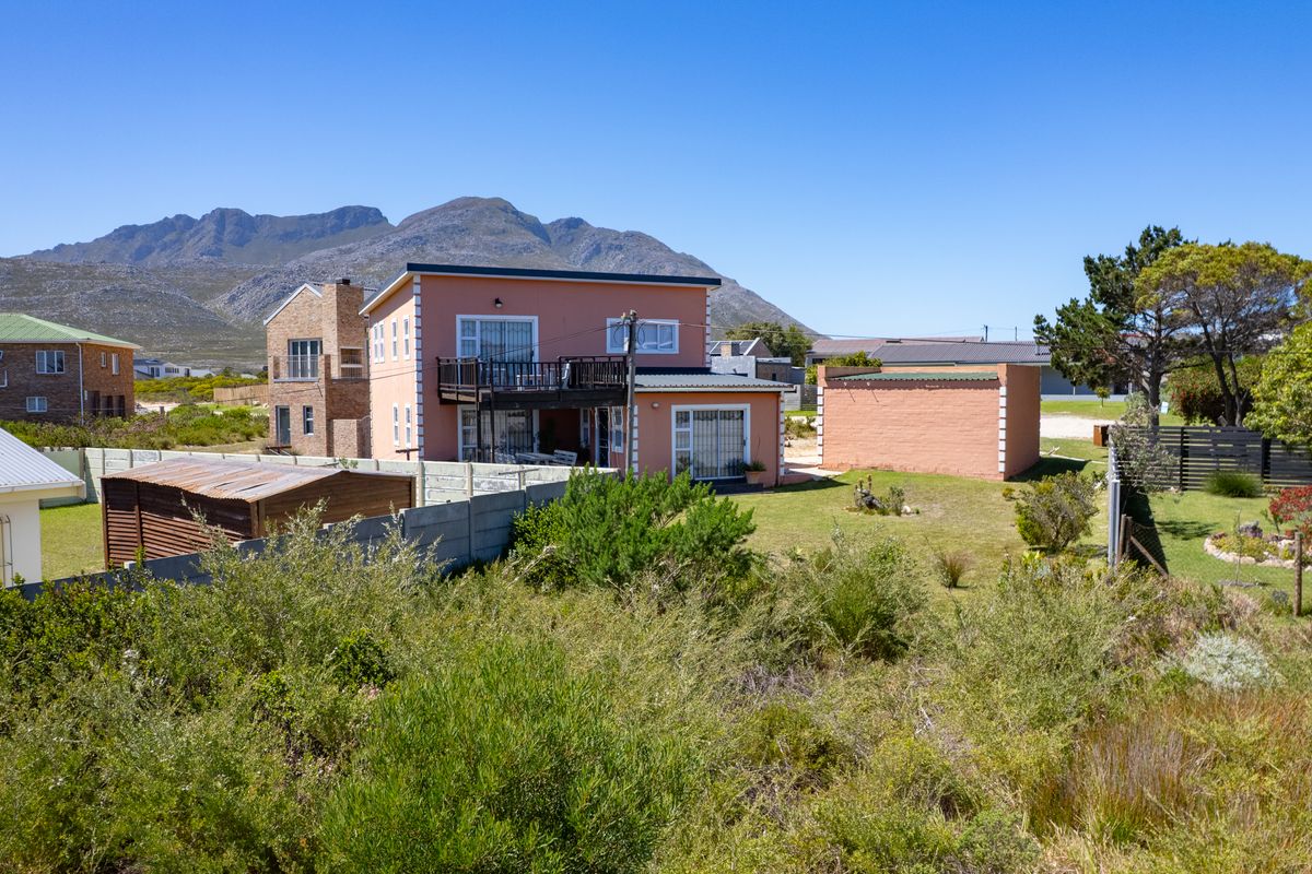 Rear view of a residential property featuring a balcony, detached garage, and established garden with mountain views in the background.