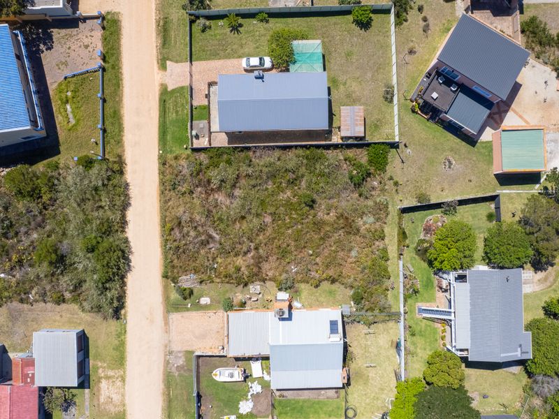 Aerial view of a vacant residential plot situated within an established neighborhood, featuring natural vegetation and surrounding boundary fencing.