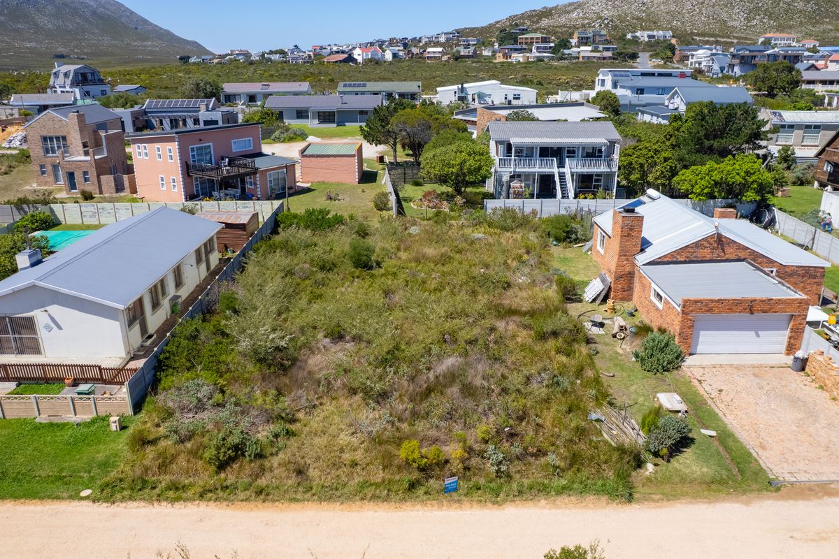 An aerial view of a vacant residential plot situated between existing homes, featuring natural vegetation and established boundary fencing.