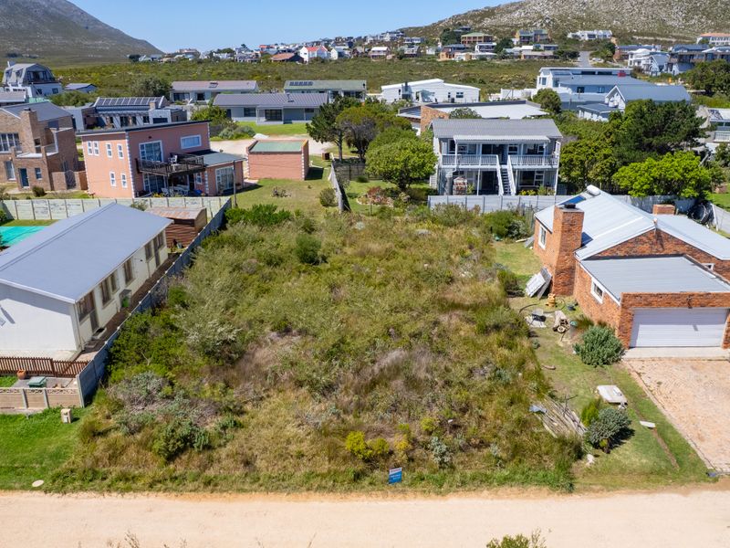 An aerial view of a vacant residential plot situated between existing homes, featuring natural vegetation and established boundary fencing.