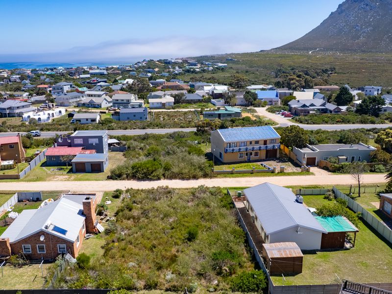 Aerial view of a residential vacant land plot situated in a coastal neighborhood with mountain views and surrounding established homes.