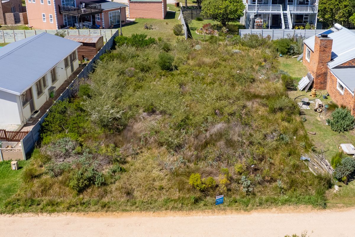 An aerial view of a vacant residential plot situated between existing neighboring properties, featuring established boundary fencing and significant natural vegetation cover.