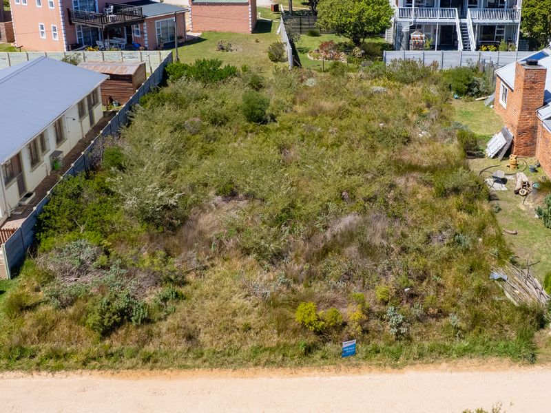 An aerial view of a vacant residential plot situated between existing neighboring properties, featuring established boundary fencing and significant natural vegetation cover.