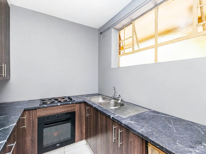 A compact kitchen featuring dark wood cabinetry, marble-effect laminate countertops, a built-in oven, electric hob, and a stainless steel double sink.