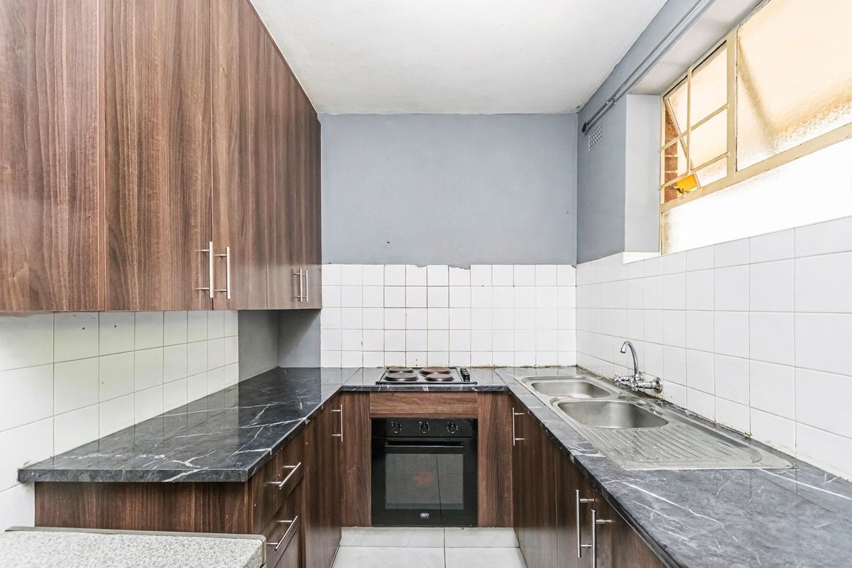 A compact kitchen featuring dark wood-look cabinetry, marble-effect laminate countertops, a built-in oven with electric hob, and a double stainless steel sink.
