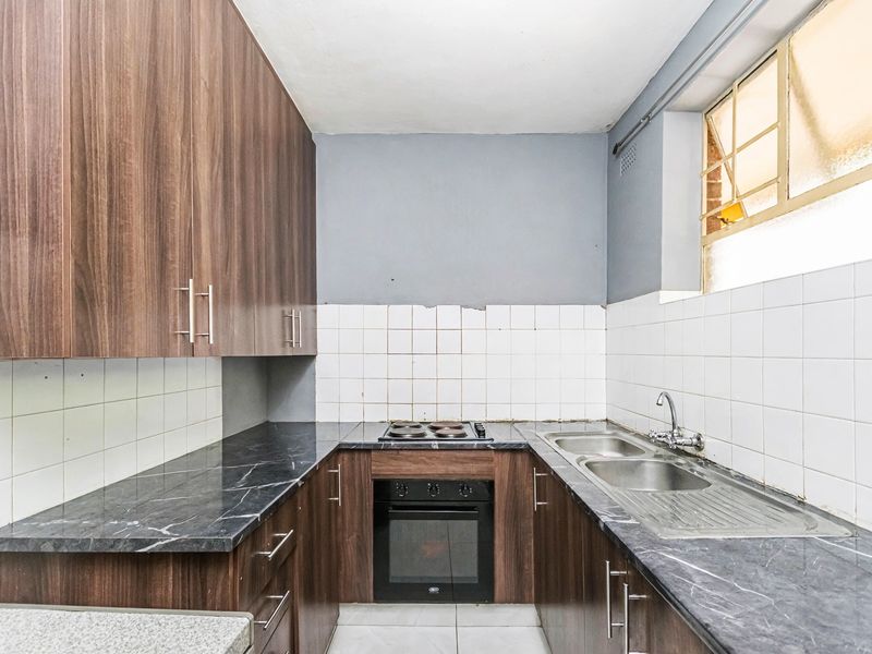 A compact kitchen featuring dark wood-look cabinetry, marble-effect laminate countertops, a built-in oven with electric hob, and a double stainless steel sink.