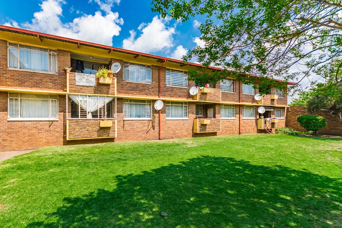 A rear view of a multi-story apartment building featuring face brick construction, individual balconies, and a well-maintained communal lawn area.