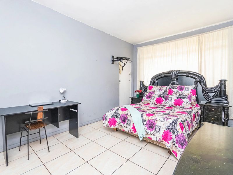 A spacious bedroom featuring neutral tiled flooring and large windows with curtain rails, offering a functional layout for a comfortable sleeping area.