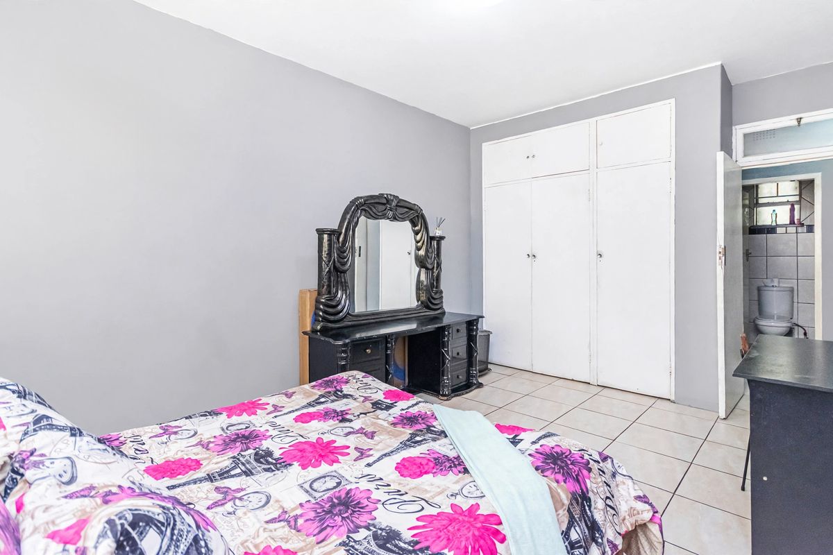 A bedroom featuring tiled flooring and built-in cupboards, with an adjacent view into a small bathroom area.