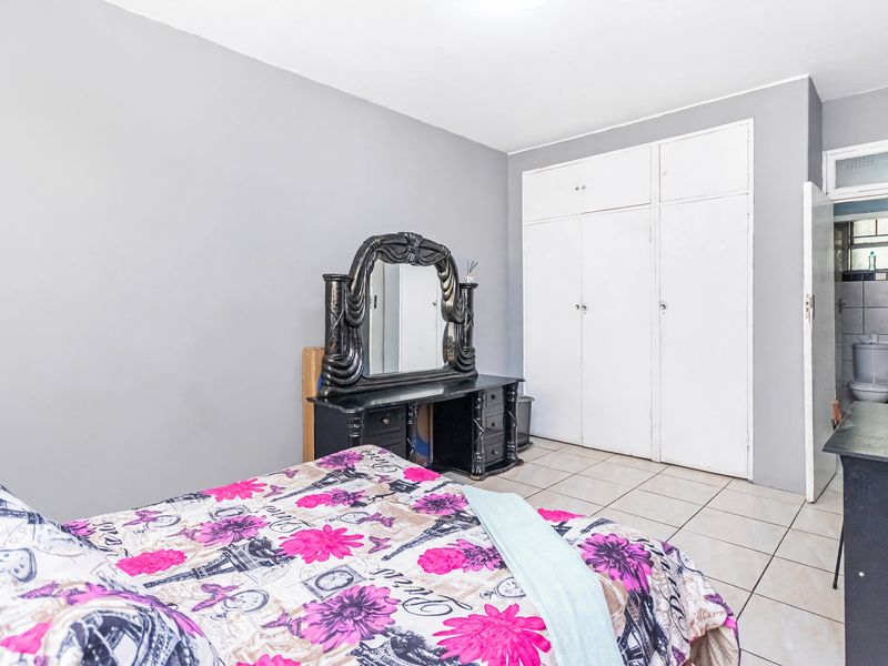 A bedroom featuring tiled flooring and built-in cupboards, with an adjacent view into a small bathroom area.