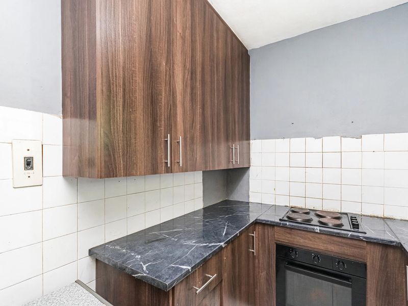 A compact kitchen featuring dark wood-look cabinetry, marble-effect laminate countertops, and a built-in electric oven and hob with a tiled backsplash.
