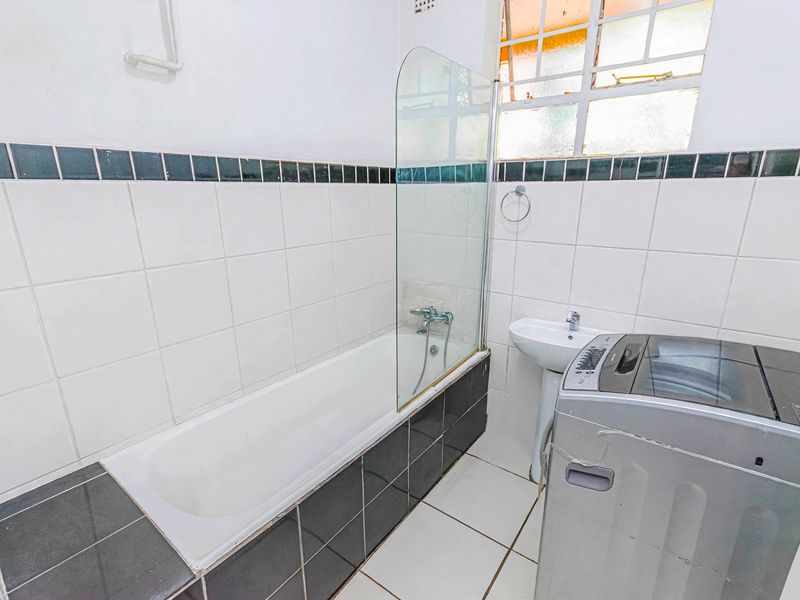 A functional bathroom featuring a bathtub with a glass screen, pedestal basin, and tiled finishes, providing a practical space for daily use.