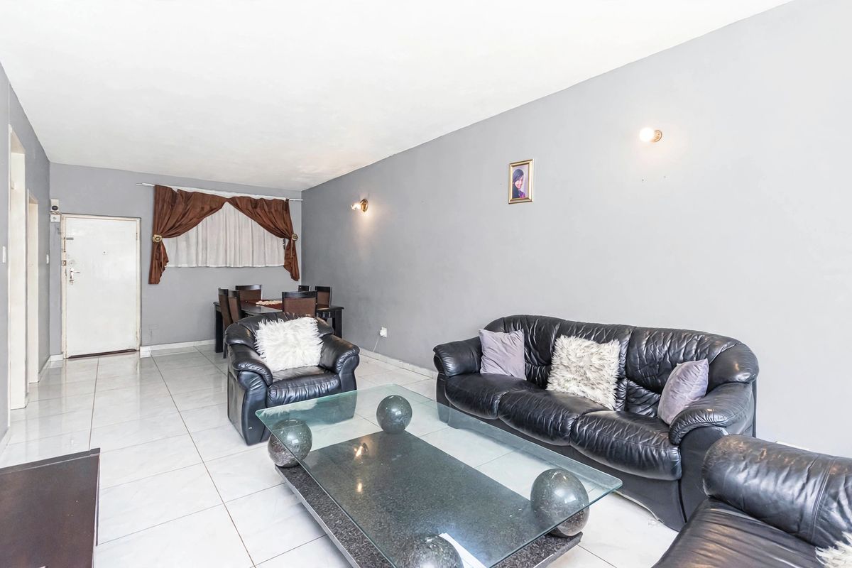 Spacious living area featuring neutral tiled flooring and wall-mounted lighting, offering a functional layout suitable for comfortable daily living.