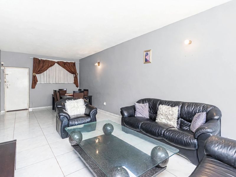 Spacious living area featuring neutral tiled flooring and wall-mounted lighting, offering a functional layout suitable for comfortable daily living.