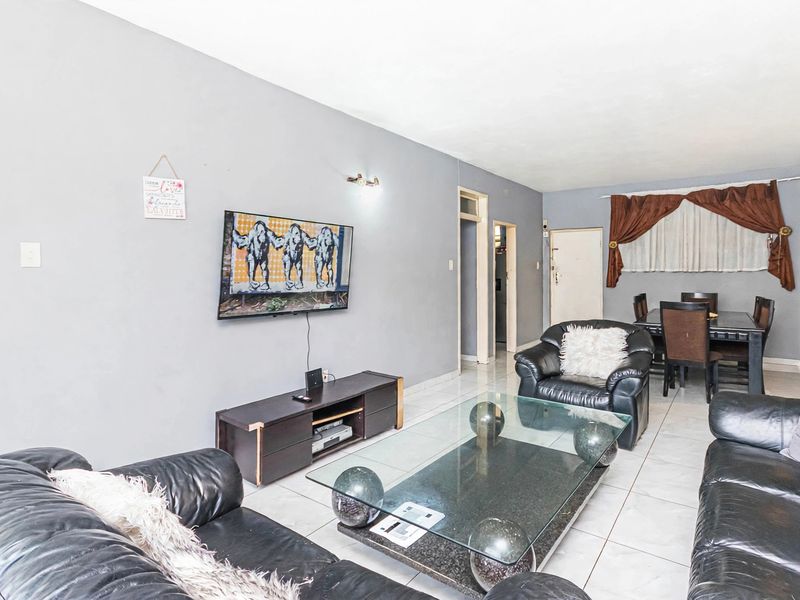 Spacious open-plan living and dining area featuring neutral grey walls and light-colored floor tiles, providing a versatile layout for modern living.