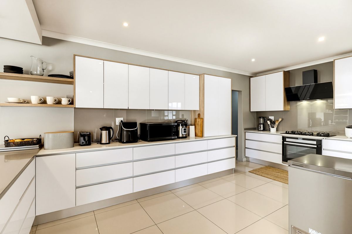 Modern kitchen featuring sleek white cabinetry, stone countertops, integrated appliances, and high-quality tiled flooring with recessed lighting.
