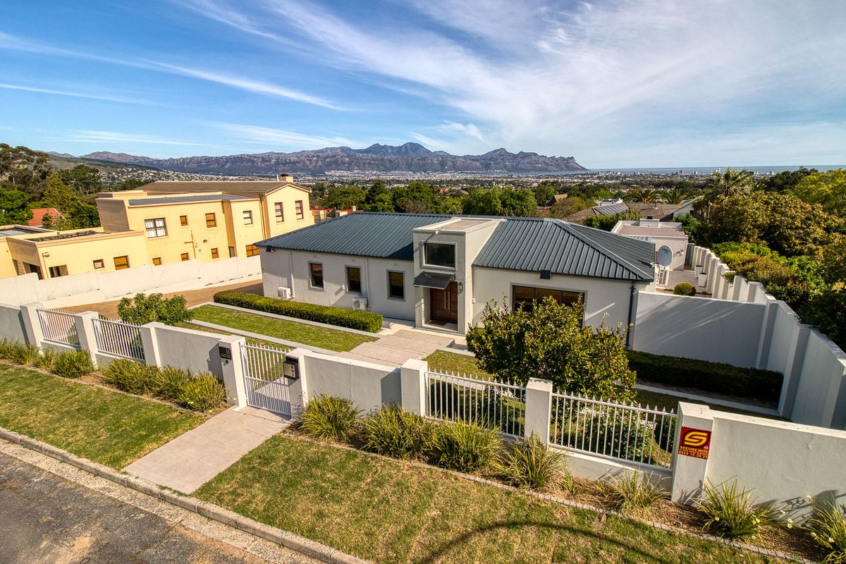 Aerial view of a modern single-story residence featuring a metal roof, secure perimeter walling, and a well-maintained garden with mountain views.