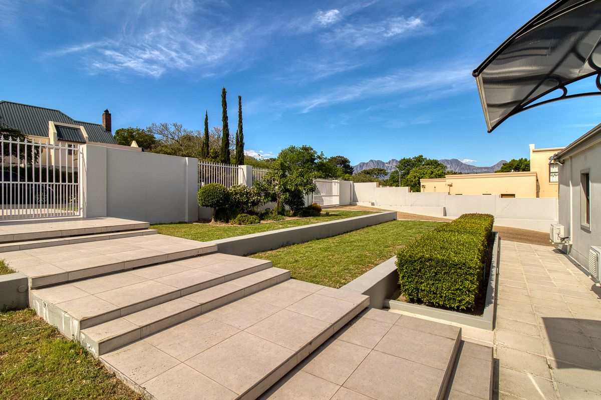 A well-maintained rear garden featuring tiered tiled steps, landscaped lawn, and secure perimeter walling with mountain views in the background.
