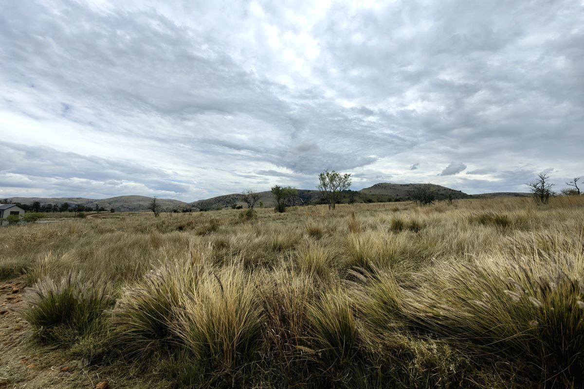 A wide-angle view of the vacant residential land featuring natural grassland and distant hills under a cloudy sky.