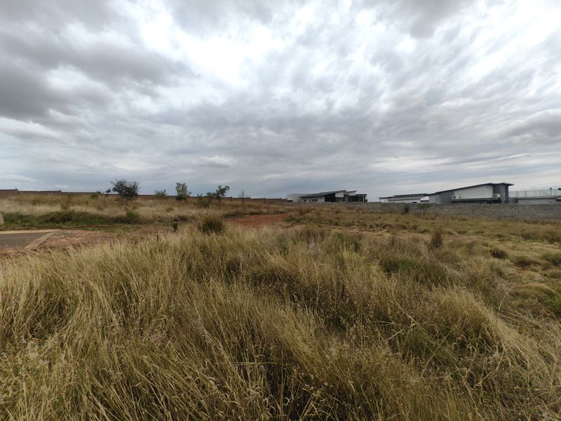 A wide-angle view of a vacant residential plot featuring natural grass cover and perimeter boundary walls.