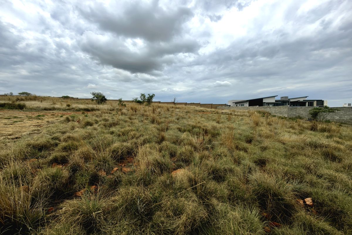 A view of a vacant residential plot featuring natural grass coverage and a perimeter boundary wall under a cloudy sky.