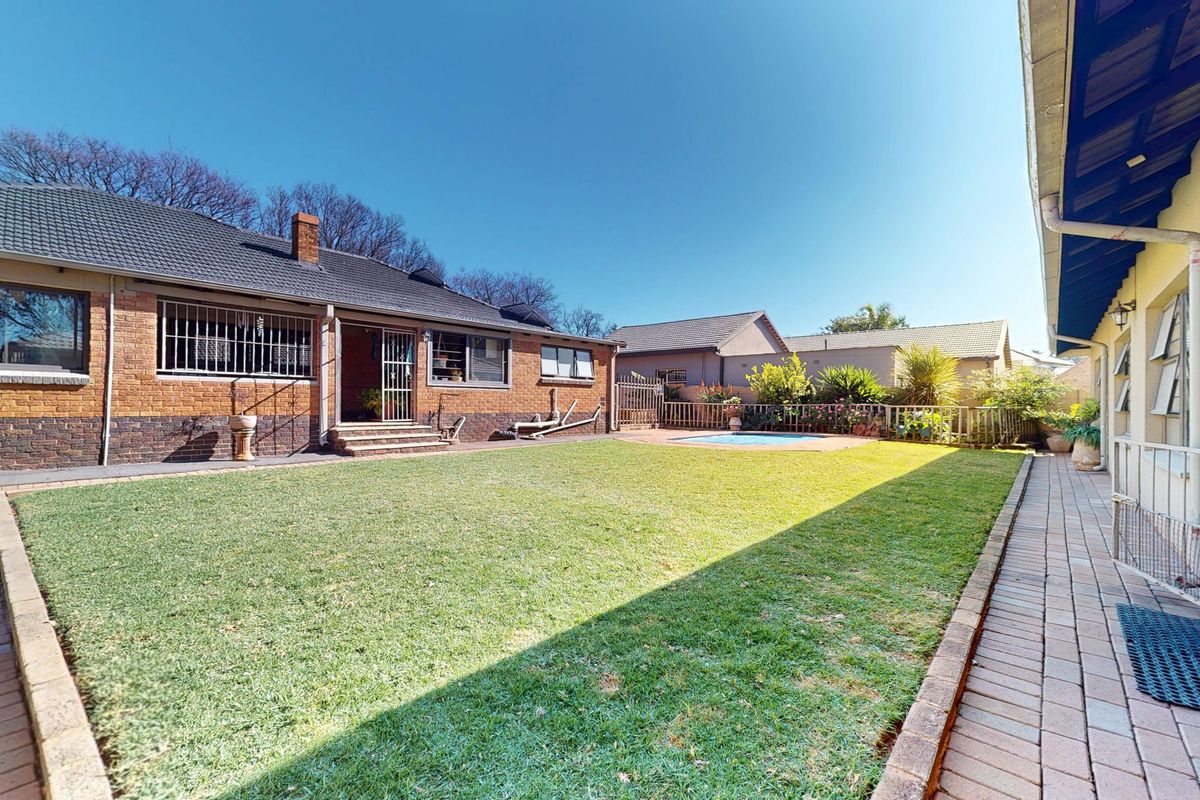 Spacious rear garden featuring a well-maintained lawn, paved patio area, and a swimming pool, set against a classic brick house exterior.