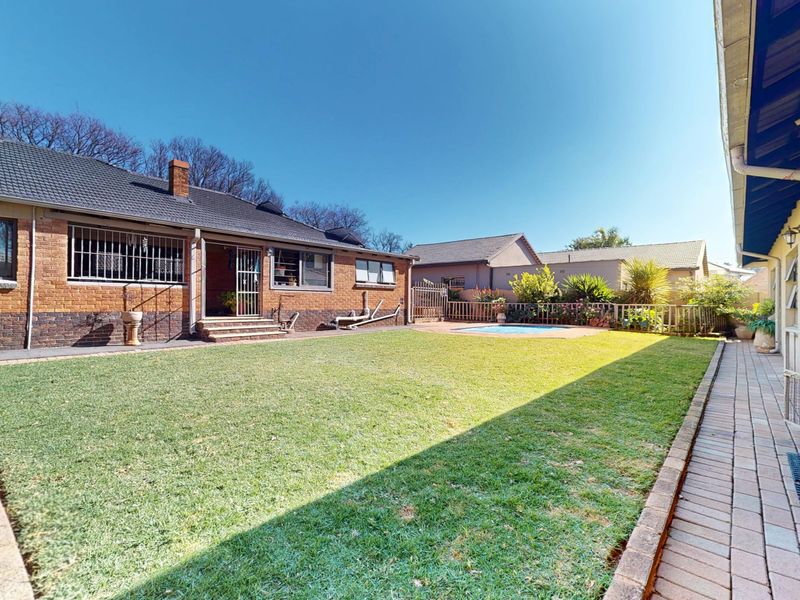 Spacious rear garden featuring a well-maintained lawn, paved patio area, and a swimming pool, set against a classic brick house exterior.
