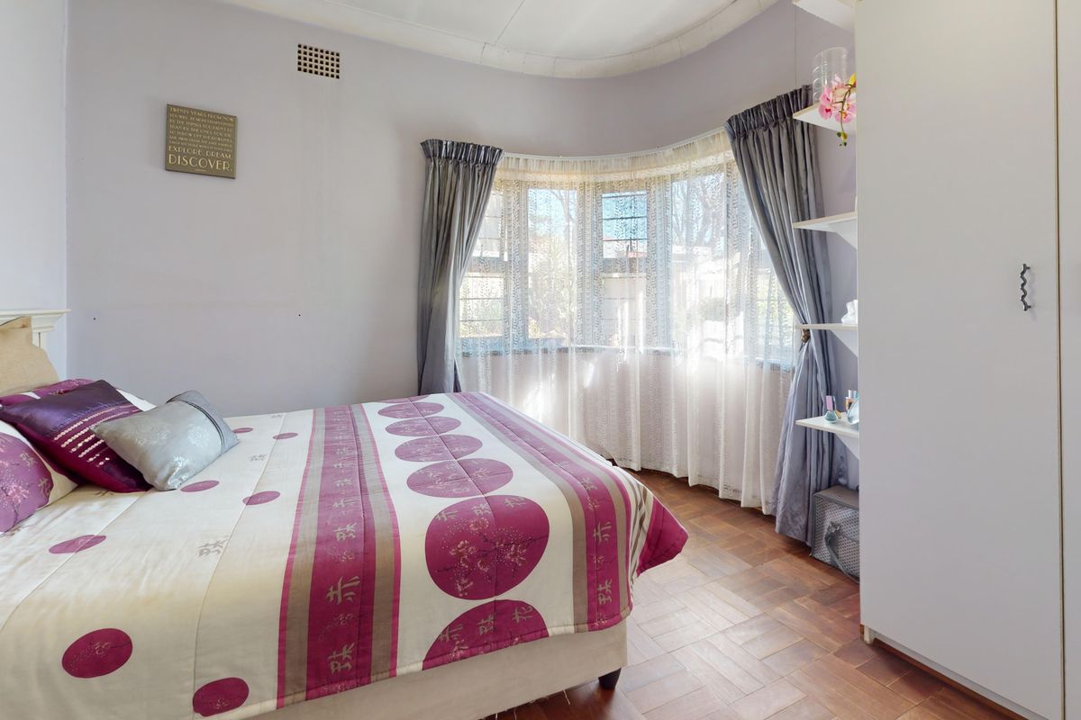 A bedroom featuring classic parquet flooring, a curved bay window, and built-in wardrobe storage, offering a bright and functional living space.