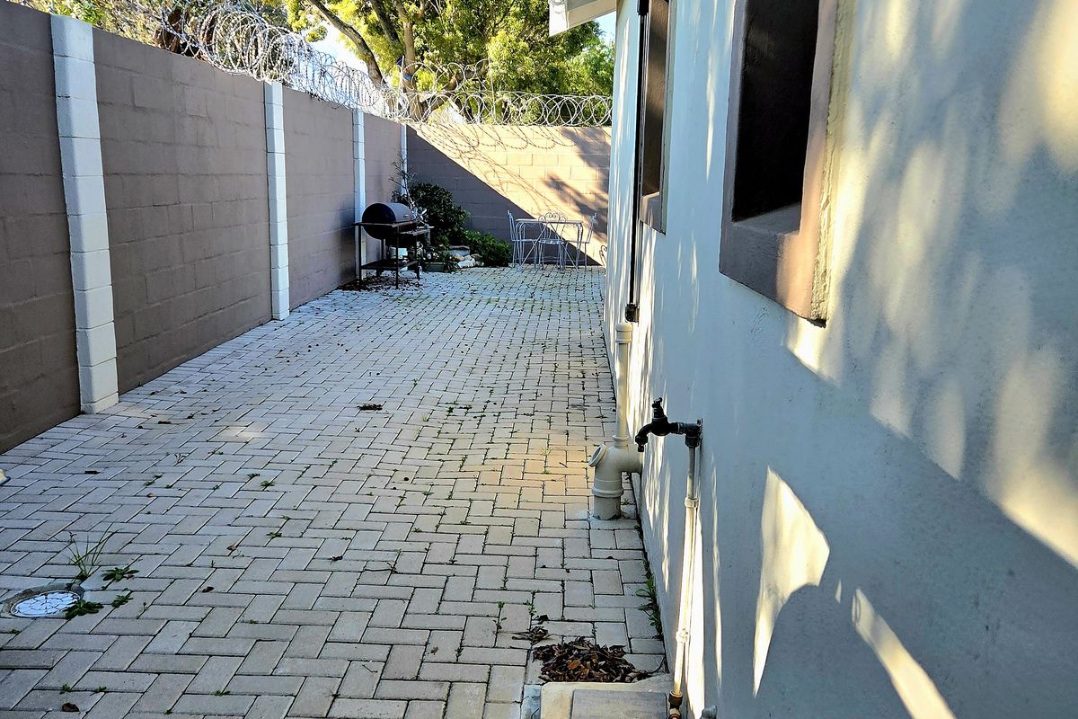 A paved side or rear exterior walkway featuring a perimeter wall with security razor wire and an external water tap.