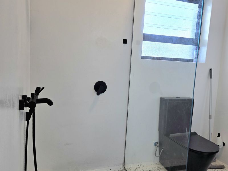Modern bathroom featuring a walk-in shower with black fixtures, a frameless glass screen, and a contemporary black toilet set against terrazzo-style flooring.