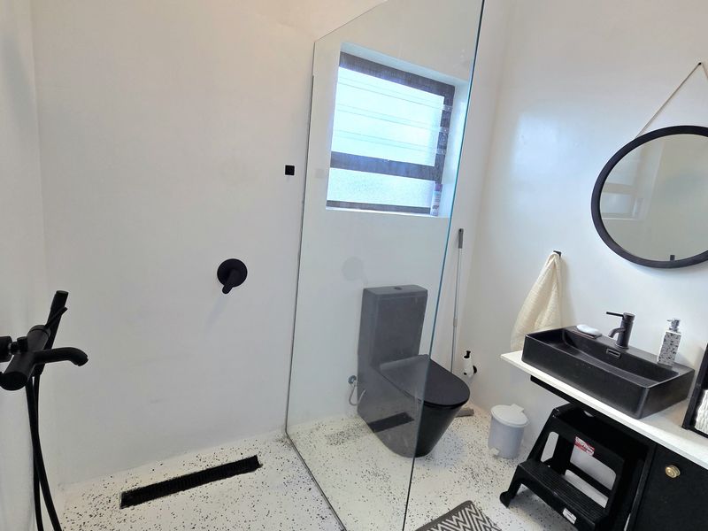 Modern bathroom featuring a walk-in shower with black fixtures, a sleek black basin vanity, and contemporary terrazzo-style flooring.