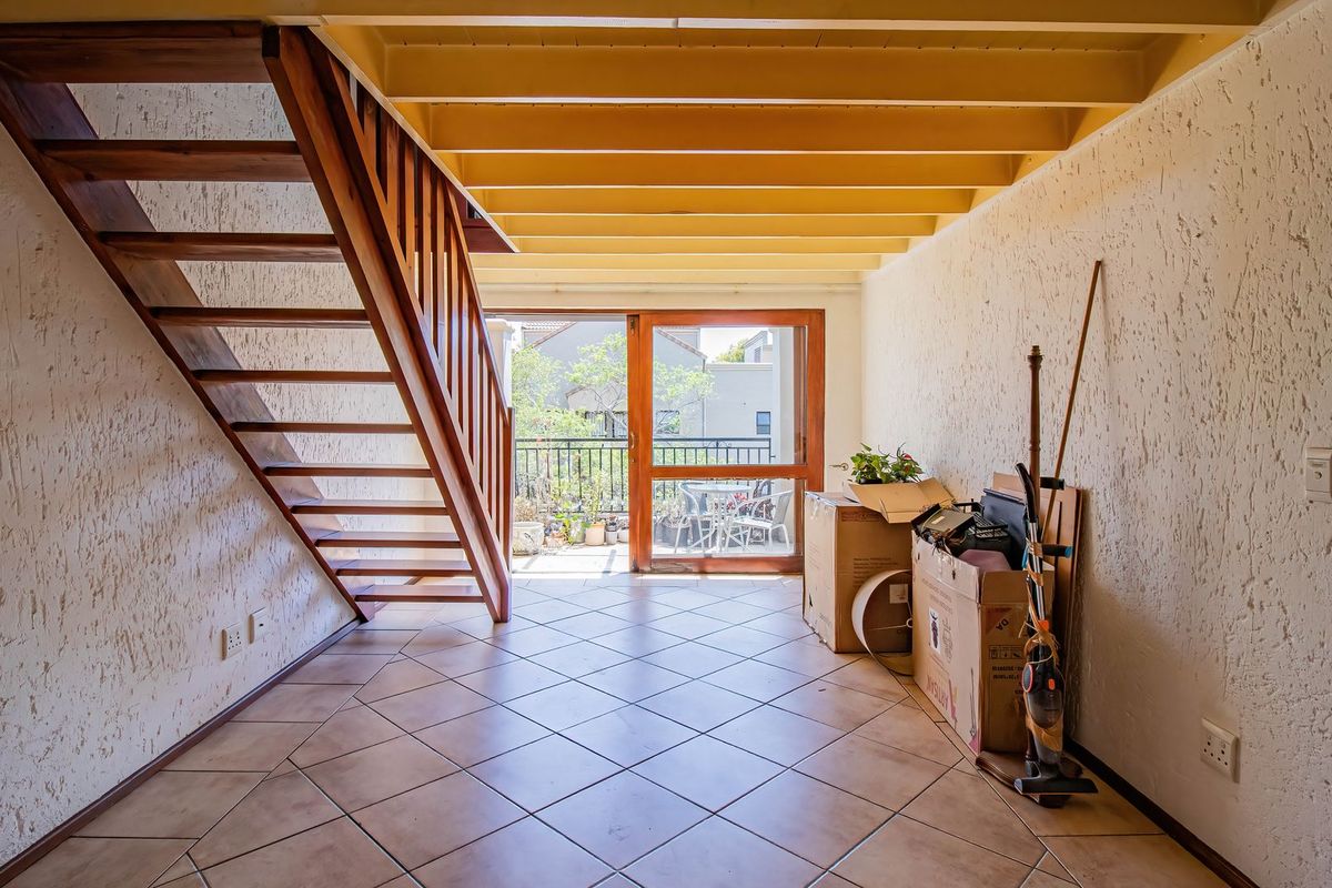 Open-plan living area featuring a wooden staircase, exposed ceiling beams, tiled flooring, and direct access to a balcony through a sliding glass door.
