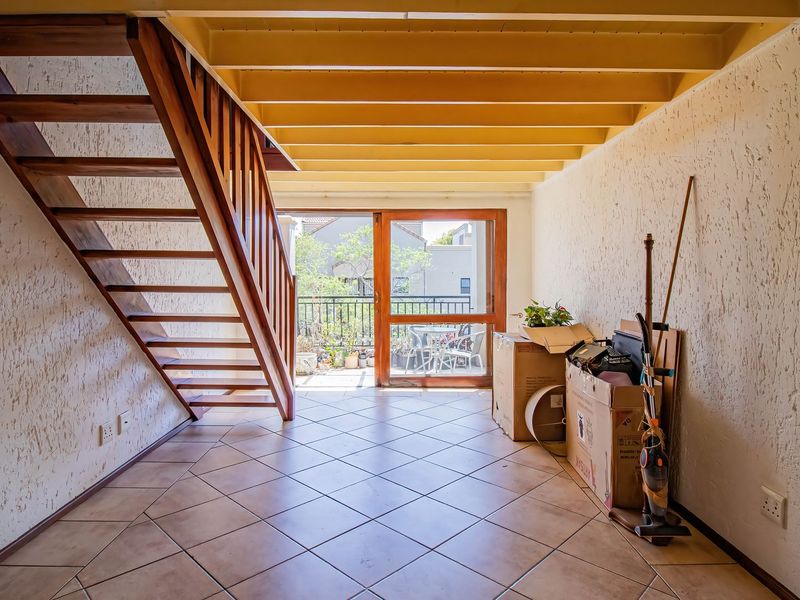 Open-plan living area featuring a wooden staircase, exposed ceiling beams, tiled flooring, and direct access to a balcony through a sliding glass door.