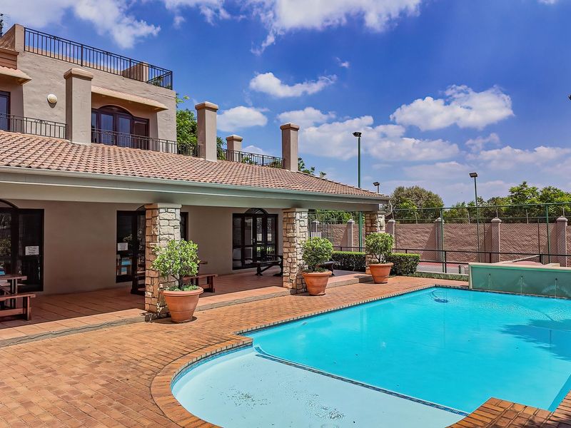 A well-maintained outdoor pool area featuring a swimming pool, covered patio with stone-clad pillars, and terracotta paving, ideal for outdoor relaxation and entertainment.