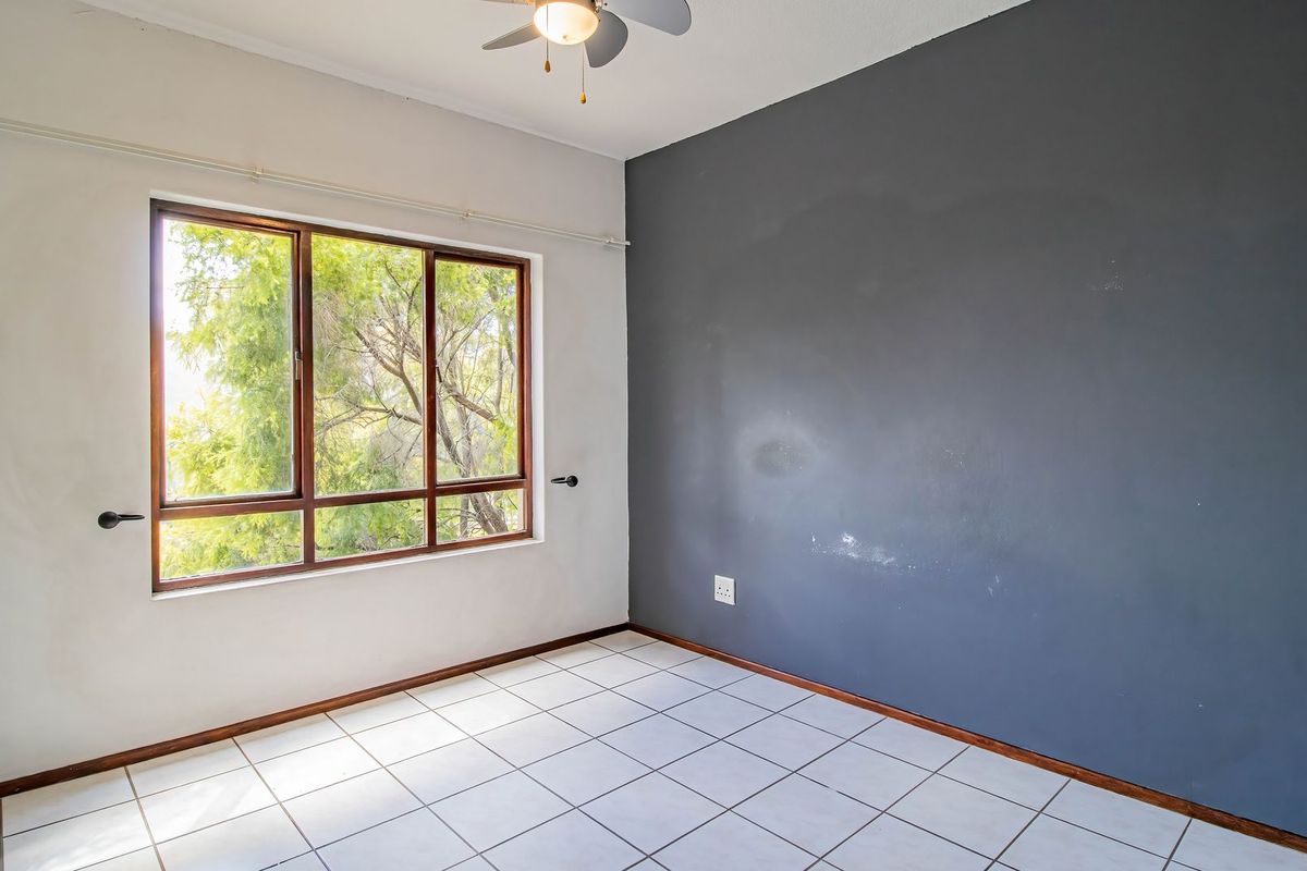 An empty bedroom featuring tiled flooring, a ceiling fan, and a large window with a view of trees.