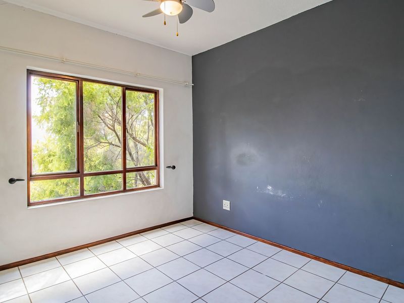 An empty bedroom featuring tiled flooring, a ceiling fan, and a large window with a view of trees.