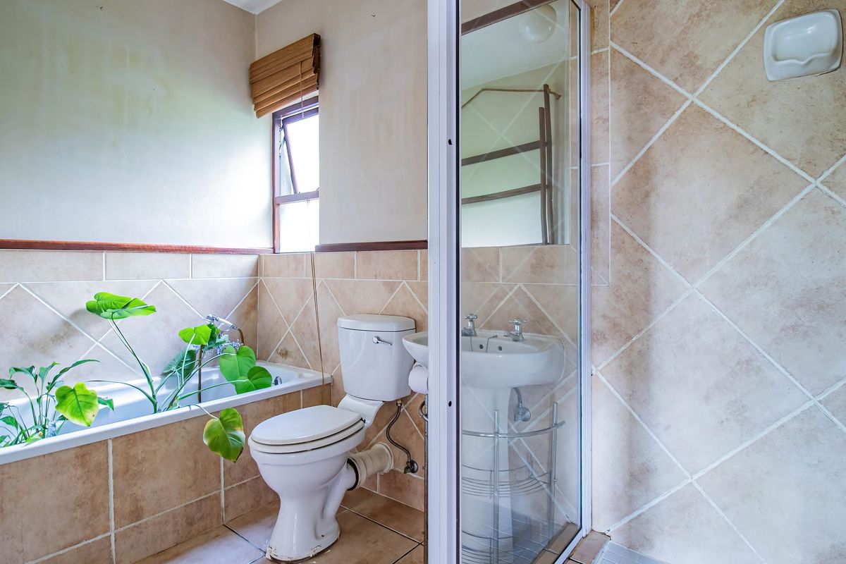 A functional bathroom featuring a bathtub, pedestal basin, toilet, and a separate shower enclosure with neutral ceramic tiling throughout.