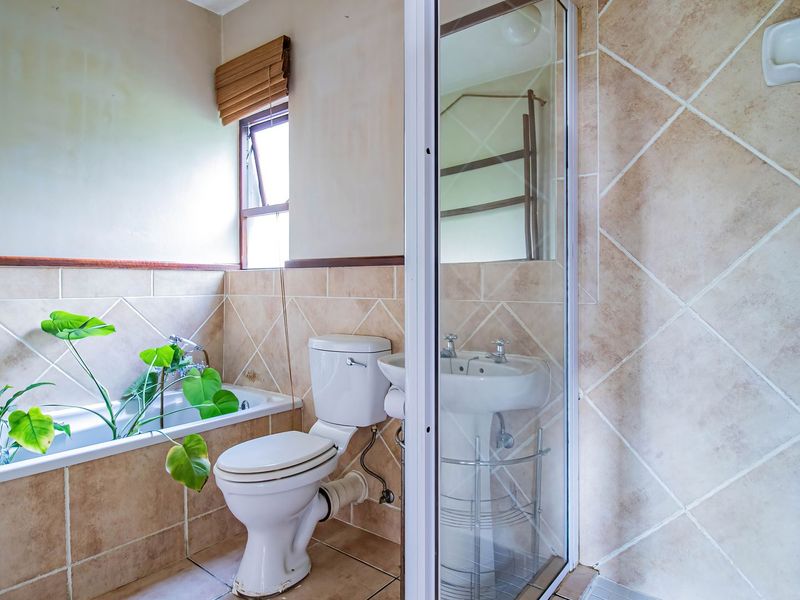 A functional bathroom featuring a bathtub, pedestal basin, toilet, and a separate shower enclosure with neutral ceramic tiling throughout.