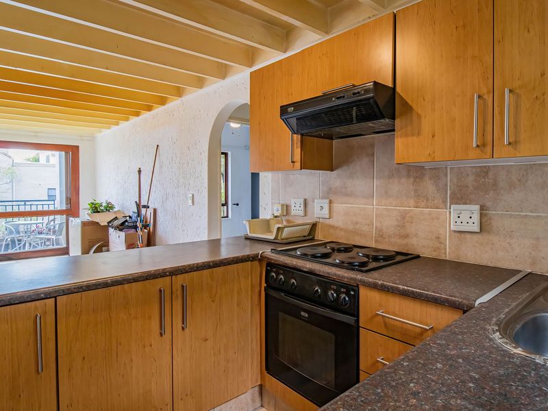 Functional kitchen featuring wooden cabinetry, laminate countertops, built-in oven, and an exposed beam ceiling, with direct access to an outdoor patio area.