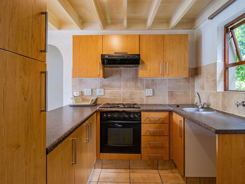 A functional kitchen featuring wooden cabinetry, built-in oven with gas hob, extractor fan, tiled backsplash, and exposed beam ceiling, offering a classic, practical layout.
