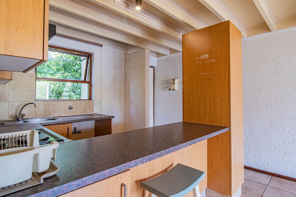 A functional kitchen featuring laminate cabinetry, a breakfast bar, and exposed ceiling beams, offering a dated aesthetic ready for modern updates.